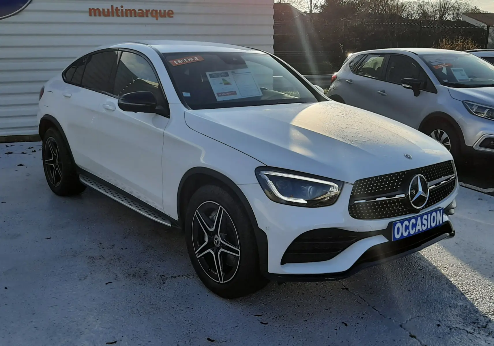 Vue avant d'une Mercedes GLC Coupé 300 4MATIC AMG Line blanche avec calandre noire et plaque "OCCASION".