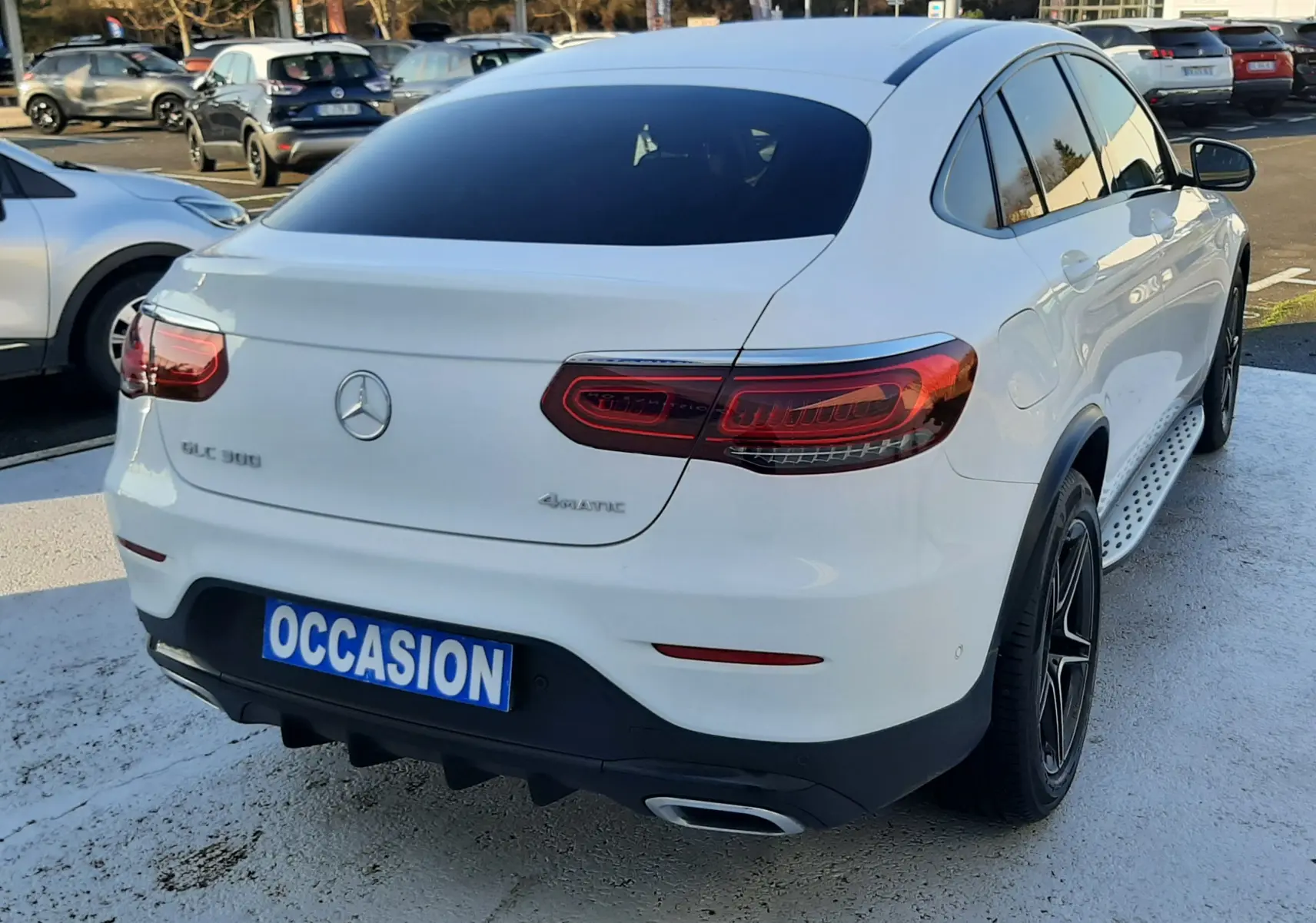 Vue arrière d'un Mercedes GLC 300 4MATIC blanc avec feux LED et plaque "OCCASION" sur parking extérieur.