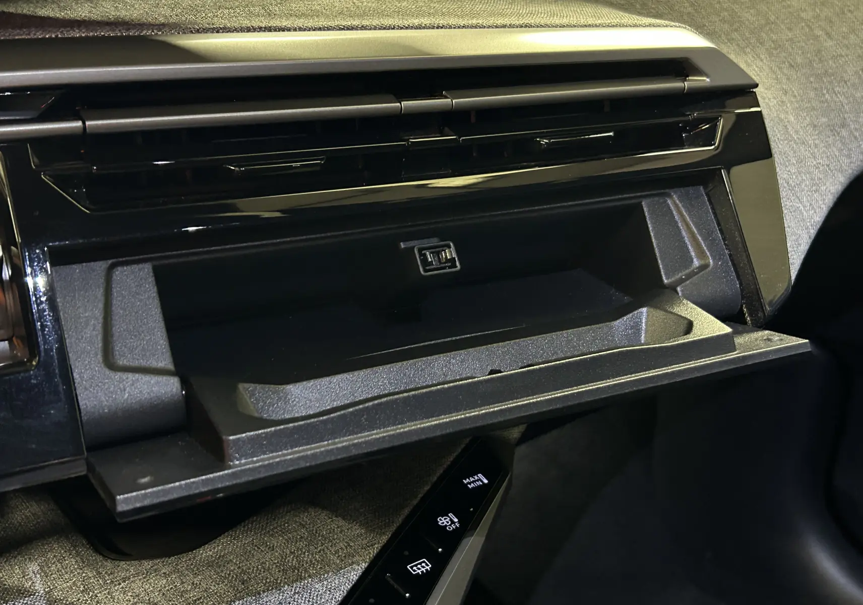 Vue rapprochée de la boîte à gants ouverte avec port USB dans l’habitacle noir du Peugeot 3008 Hybrid 2025.