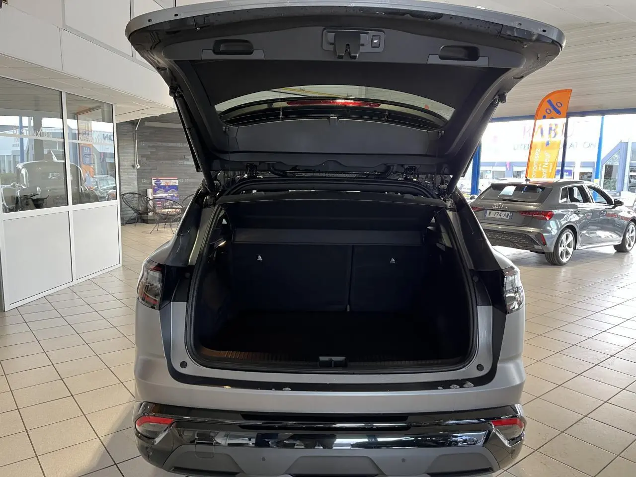 Vue arrière d’un Renault Austral gris avec hayon motorisé ouvert montrant le coffre spacieux en intérieur showroom.
