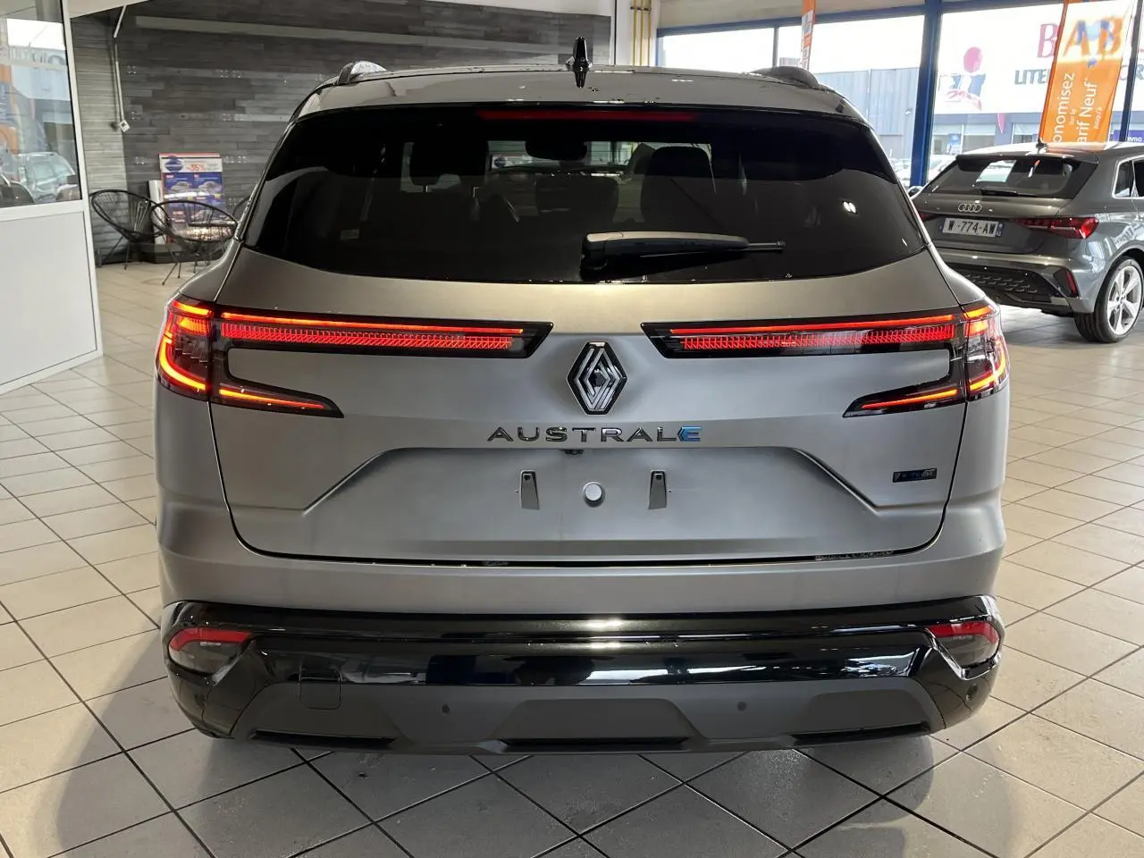 Vue arrière d'un Renault Austral gris avec feux LED allumés et hayon motorisé en intérieur showroom.