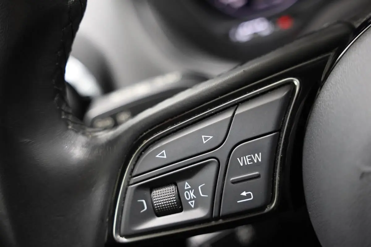 Gros plan sur les commandes au volant en cuir noir de l'Audi Q2 gris, avec boutons de navigation et fonction View.
