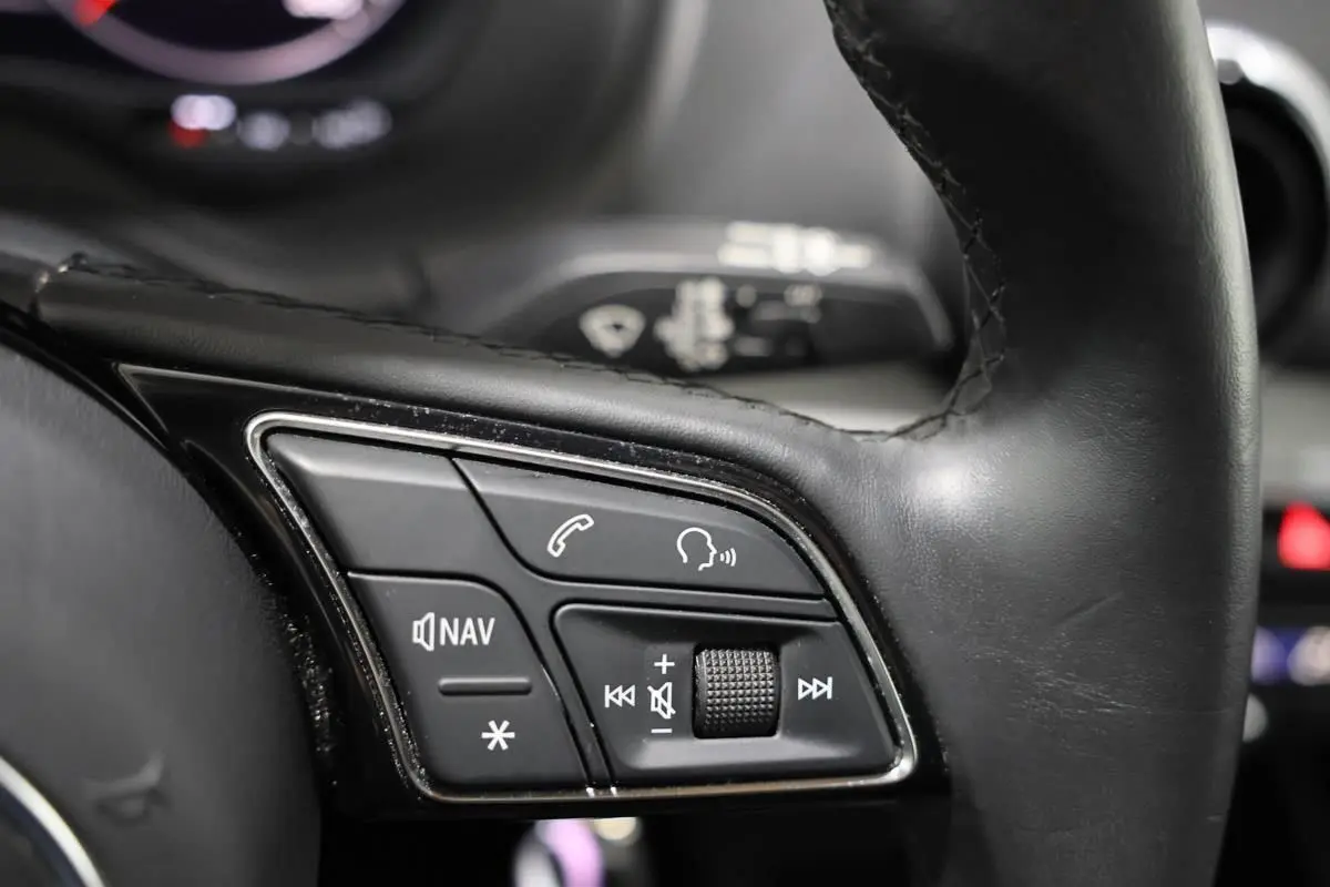 Gros plan sur les commandes multifonctions du volant en cuir noir de l’Audi Q2 TFSI 110 gris, avec boutons de navigation et volume.