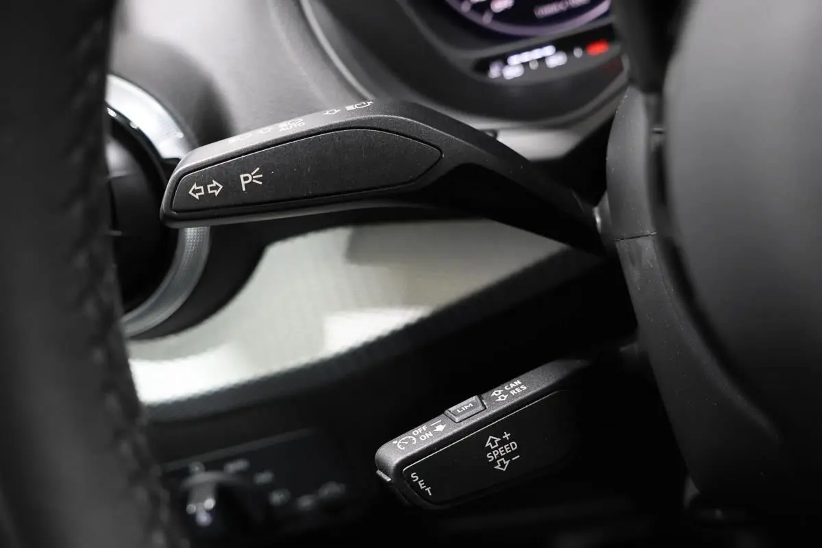 Gros plan sur les commandes au volant d’un Audi Q2 gris 2023, mettant en valeur les leviers de clignotants et régulateur de vitesse.