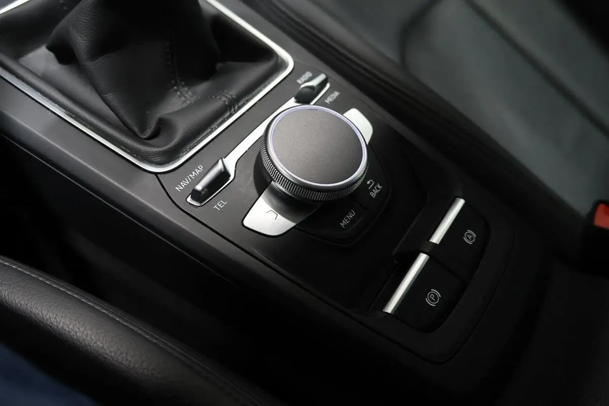 Vue rapprochée de la console centrale noire avec molette de contrôle et levier de vitesse du Audi Q2 gris.