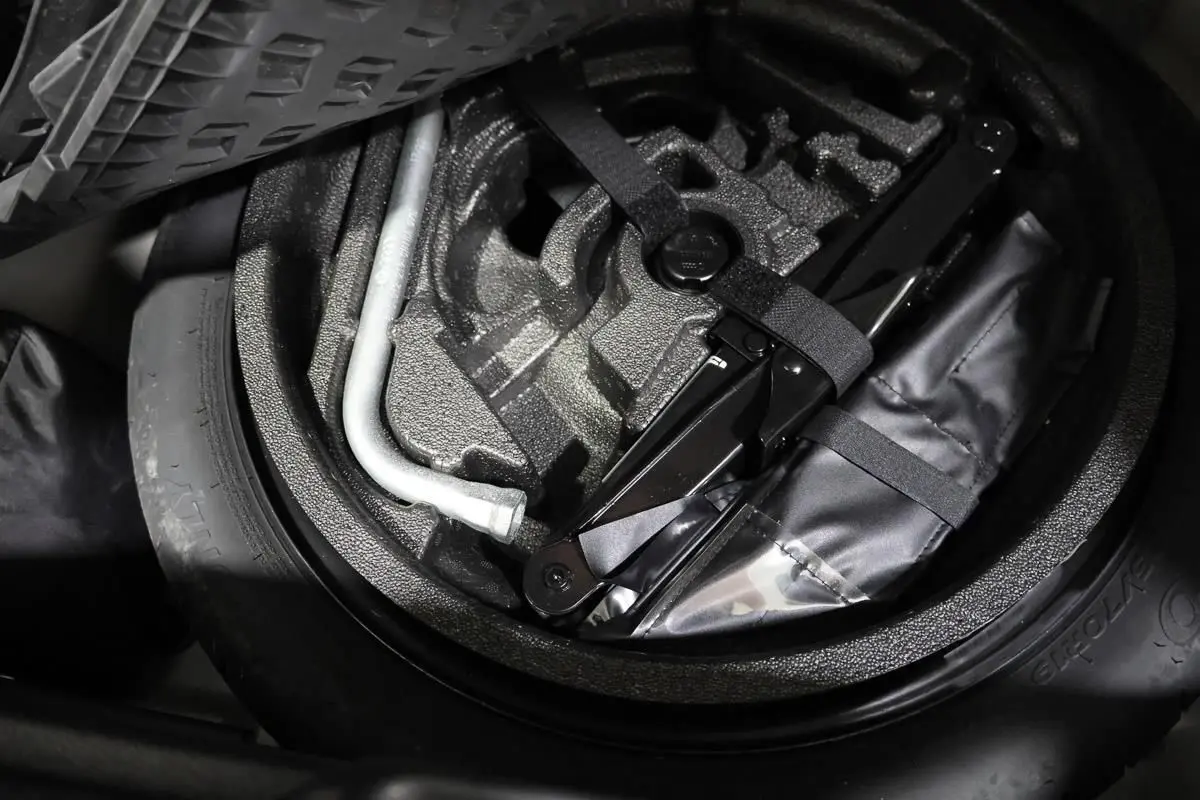 Vue rapprochée de la roue de secours et du kit de réparation dans le coffre d'un Audi Q2 gris 2023.