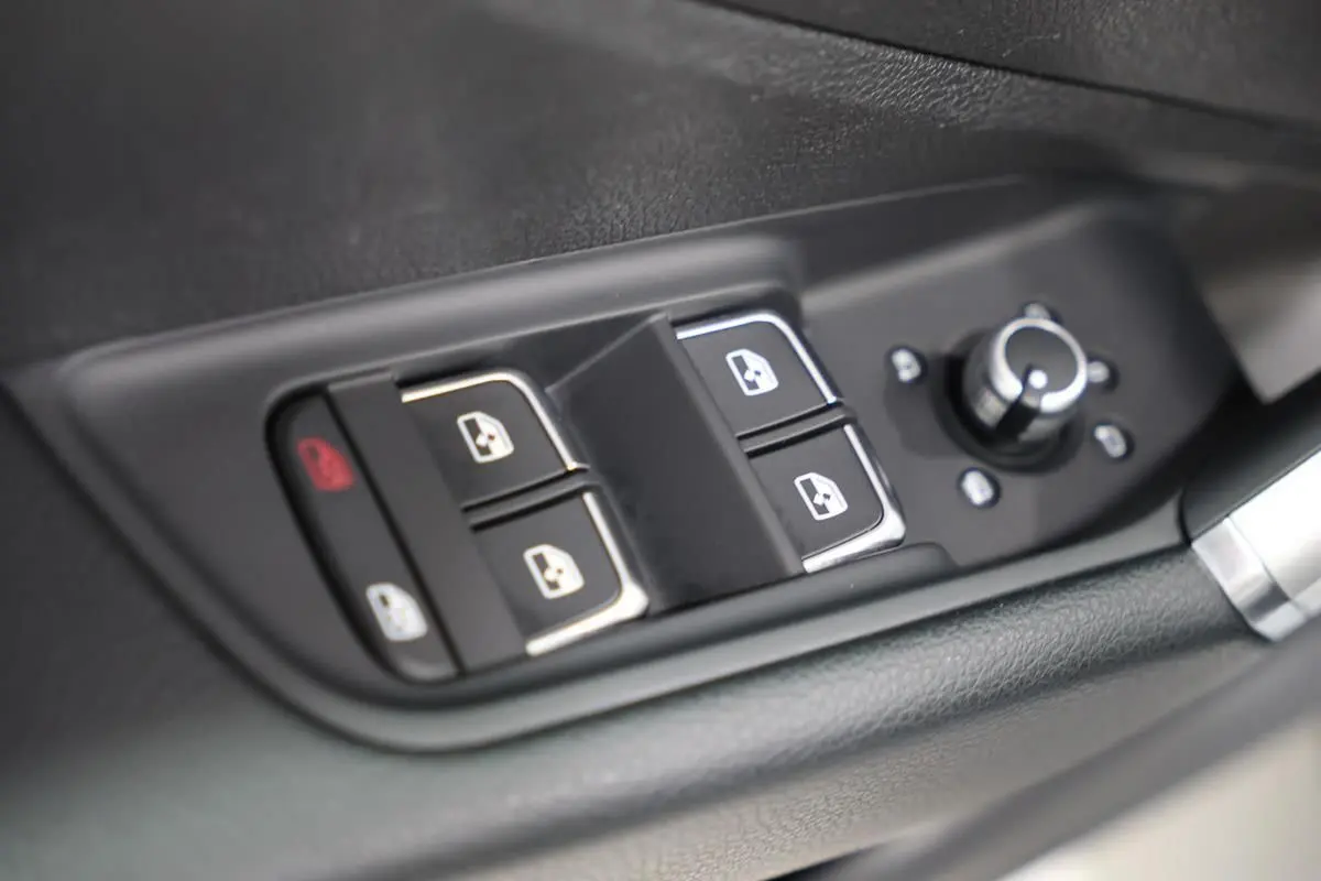 Gros plan sur les commandes de lève-vitres et réglage des rétroviseurs côté conducteur de l'Audi Q2 gris 2023.