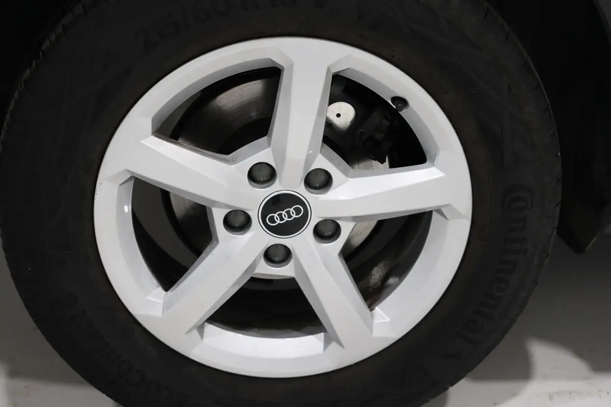 Gros plan sur la jante blanche à cinq branches d’un Audi Q2 gris, mettant en valeur le logo Audi au centre.