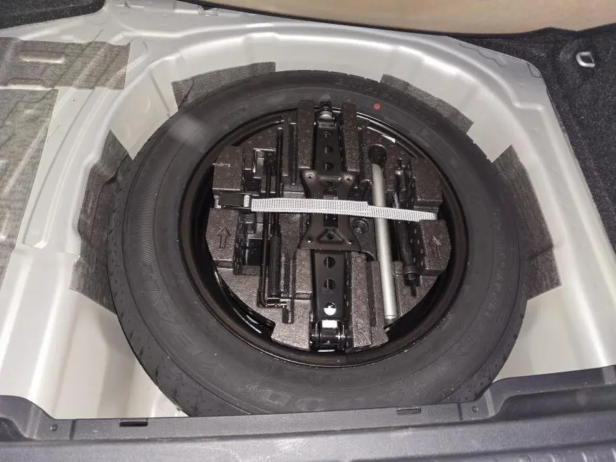 Vue plongeante sur la roue de secours noire et ses outils dans le coffre d’un Skoda Kamiq gris 2023.