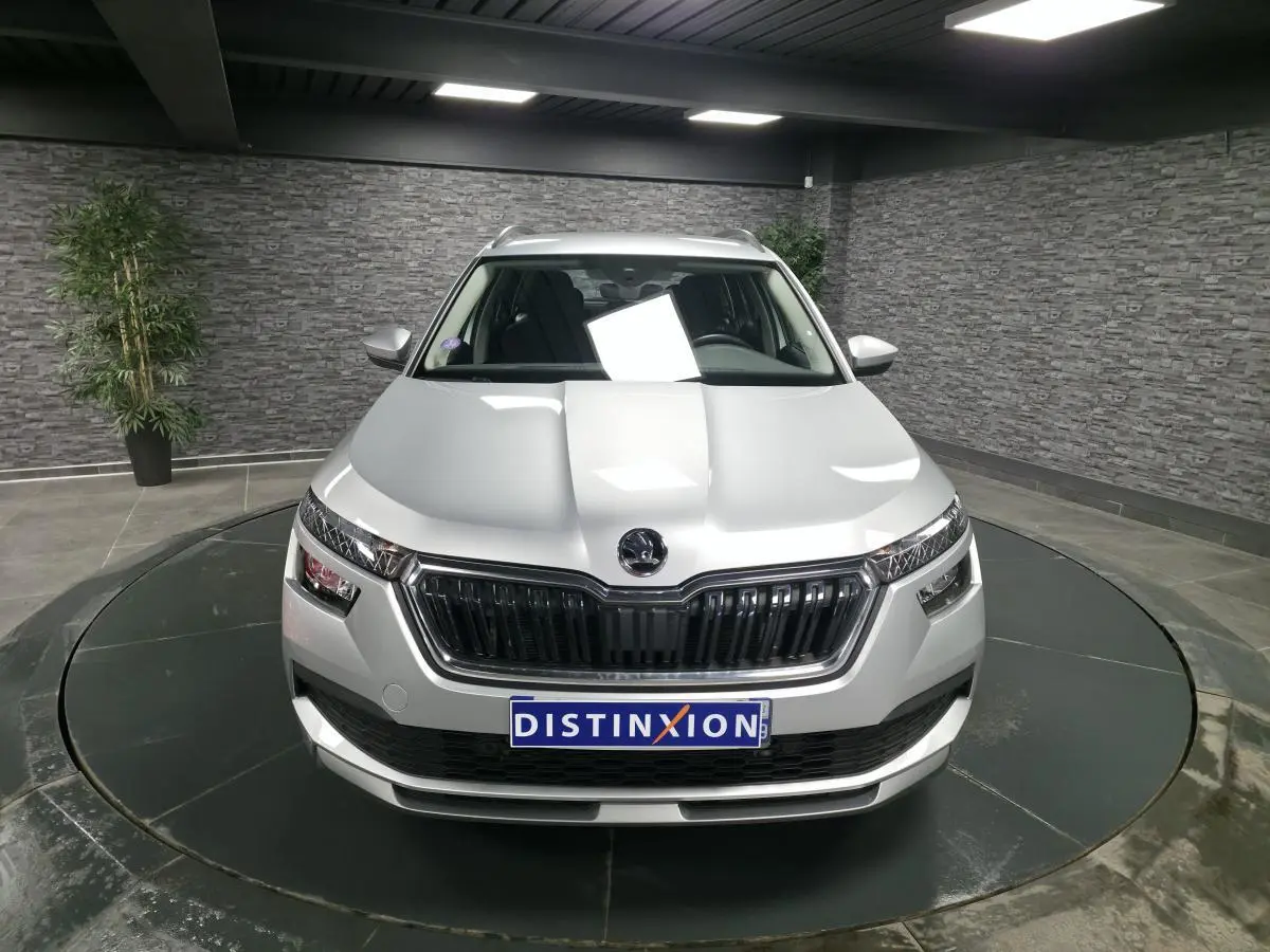 Vue avant d'un Skoda Kamiq gris métallisé avec calandre noire et plaque Distinxion en intérieur showroom.