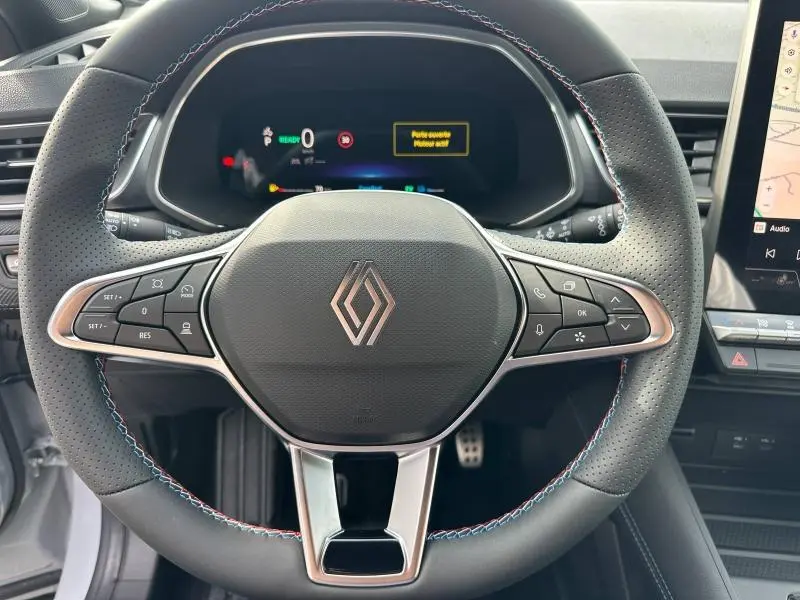 Vue rapprochée du volant perforé avec logo Renault et tableau de bord numérique du Captur hybride Gris Rafale/Noir Étoilé 2026.