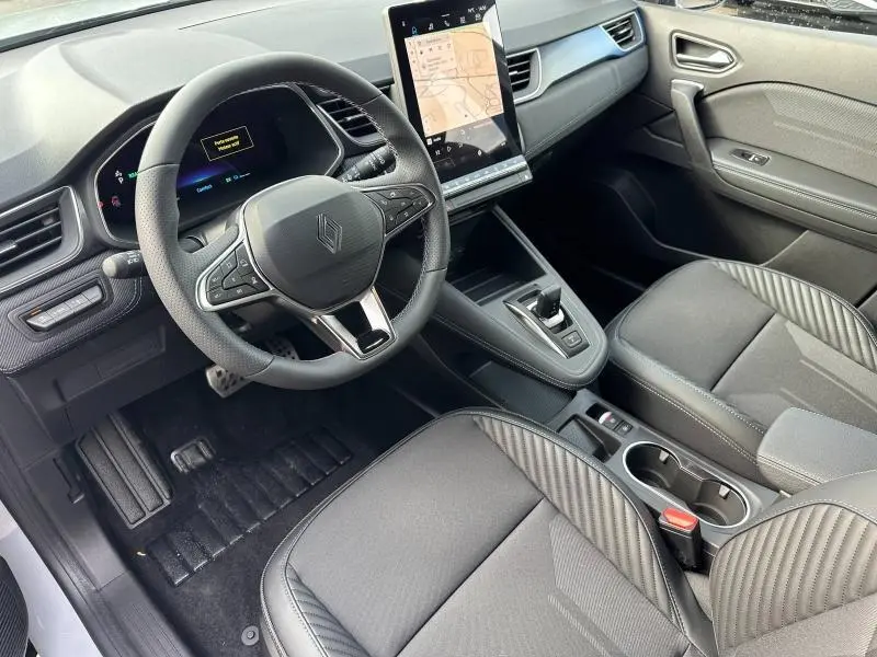 Vue intérieure côté conducteur du Renault Captur 2026 hybride, avec tableau de bord numérique et sièges gris à surpiqûres.