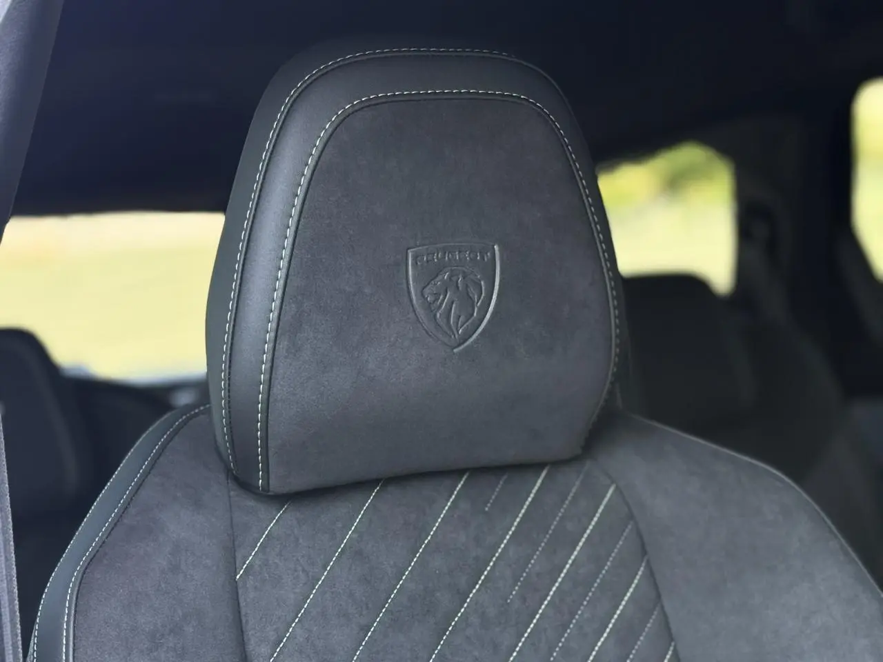 Gros plan sur l’appui-tête en Alcantara noir avec logo Peugeot embossé, intérieur du Peugeot 5008 Hybrid GT 2026.