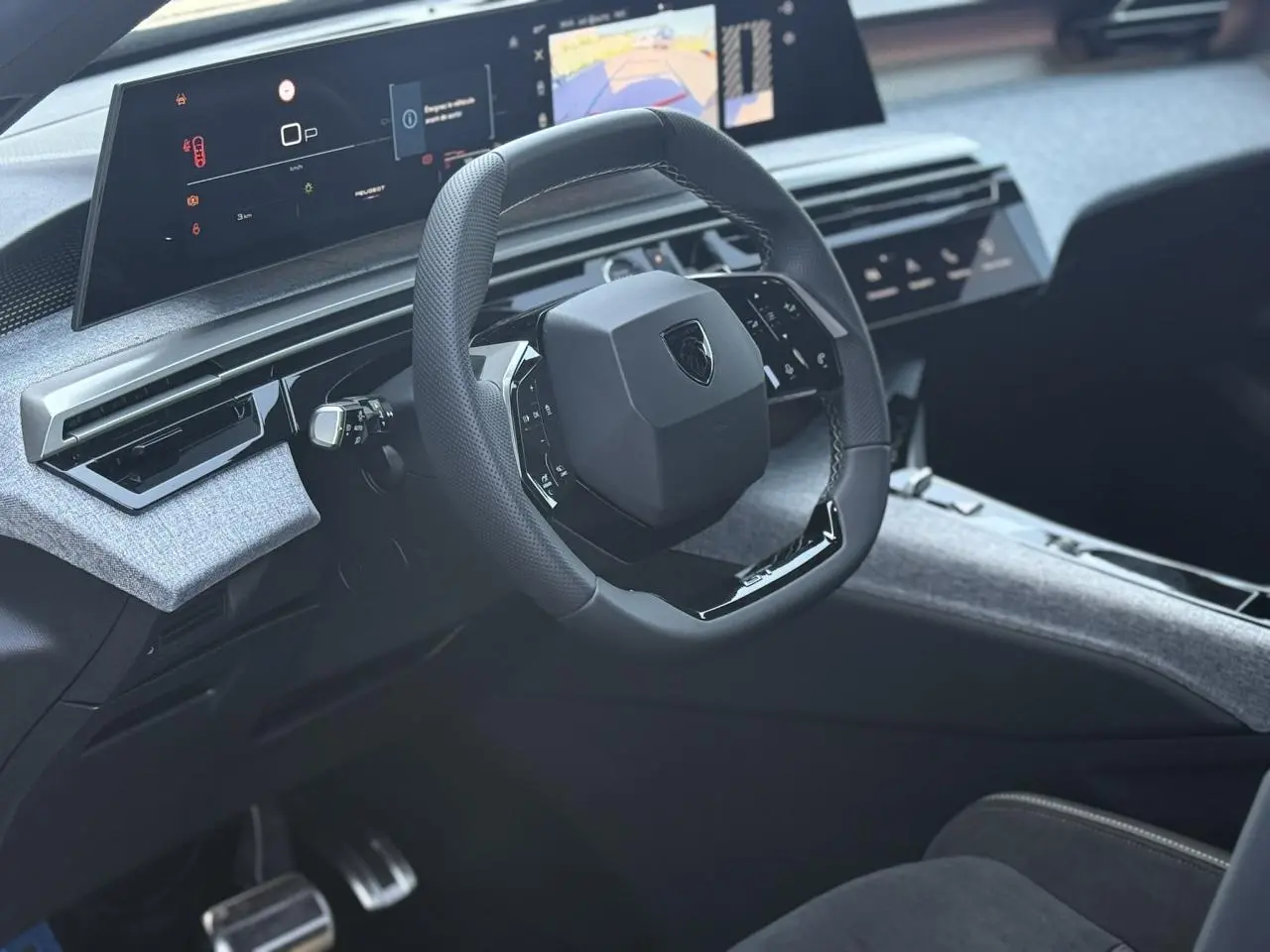 Vue intérieure du poste de conduite du Peugeot 5008 Hybrid 2026, volant compact noir laqué et tableau de bord numérique panoramique.
