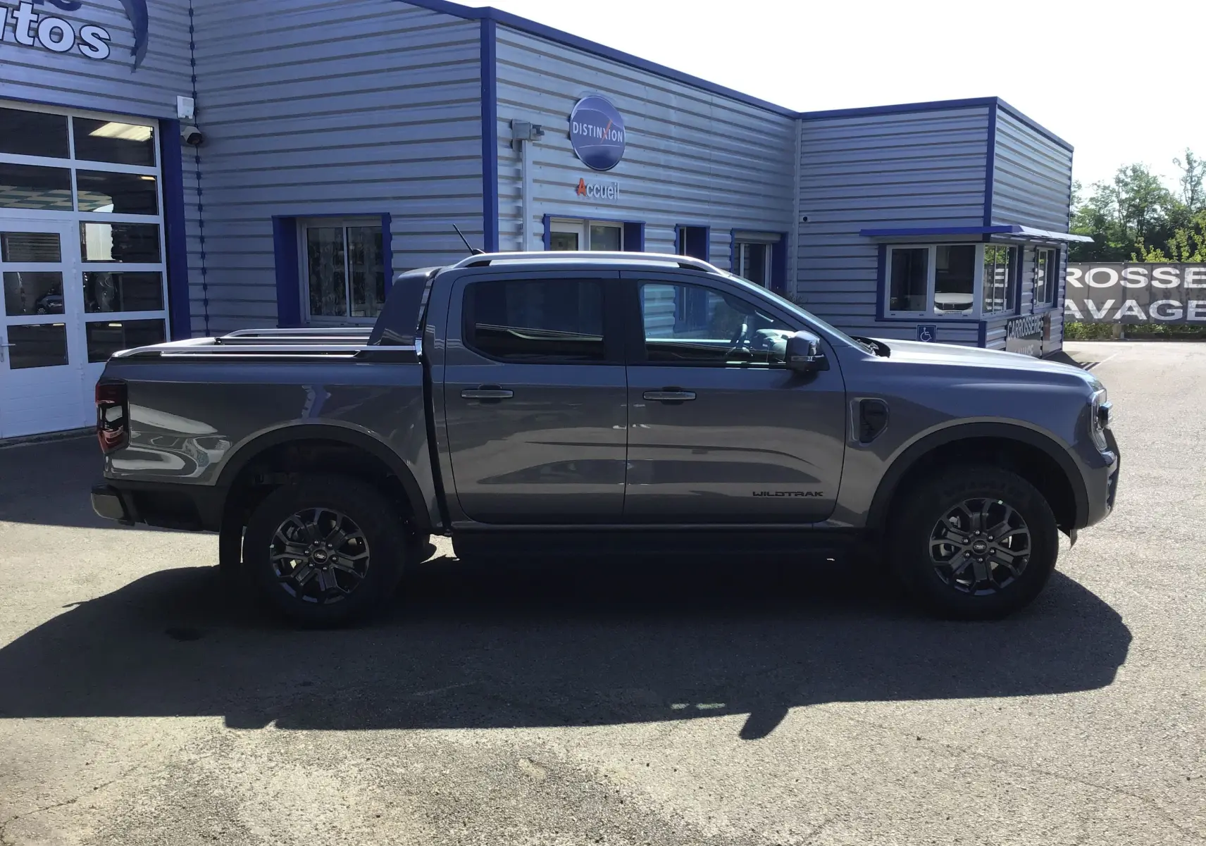 Ford Ranger Double Cabine Wildtrak gris carbone vu de profil côté gauche avec rideau de plateau coulissant et marchepied.