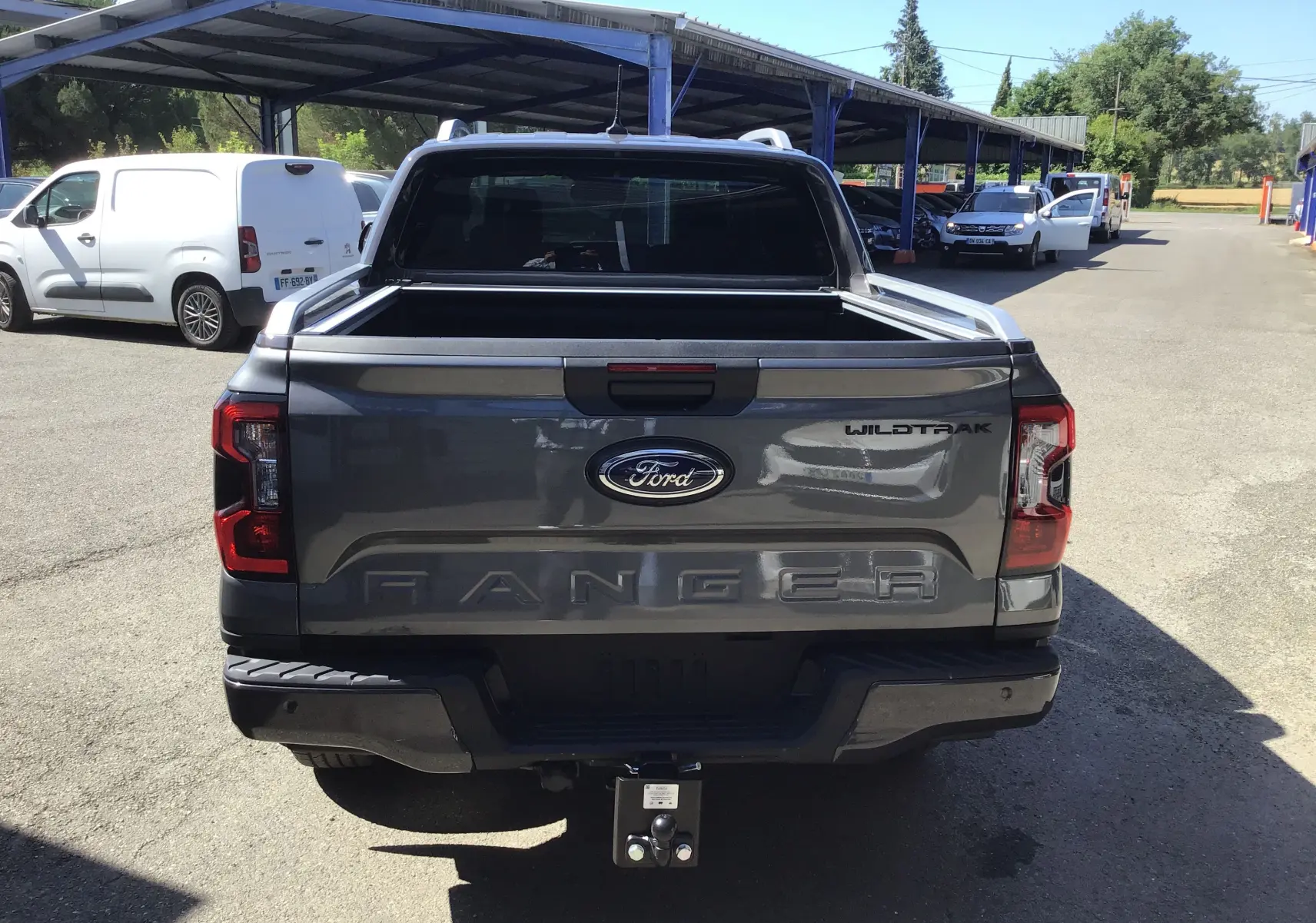 Vue arrière d'un Ford Ranger Wildtrak gris carbone avec hayon ouvert et attelage visible en extérieur.