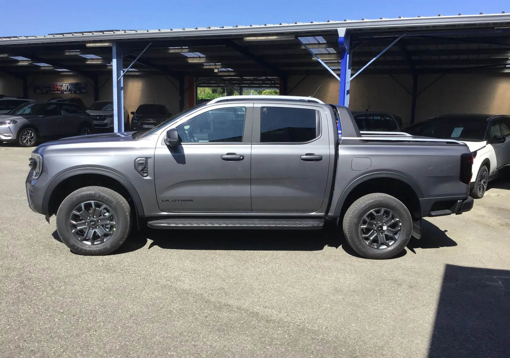 Ford Ranger Double Cabine Wildtrak gris carbone vu de profil côté gauche avec rideau de plateau électrique et marchepied visible.