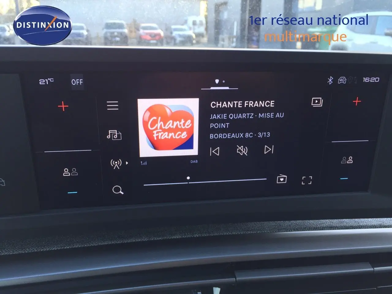 Écran tactile central du tableau de bord du Peugeot 5008 blanc, affichant la radio Chante France en extérieur urbain.