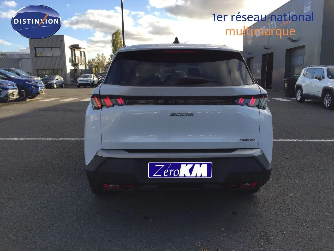 Vue arrière d'un Peugeot 5008 blanc Okenite Metal avec feux LED distinctifs et badge Hybrid sur un parking.