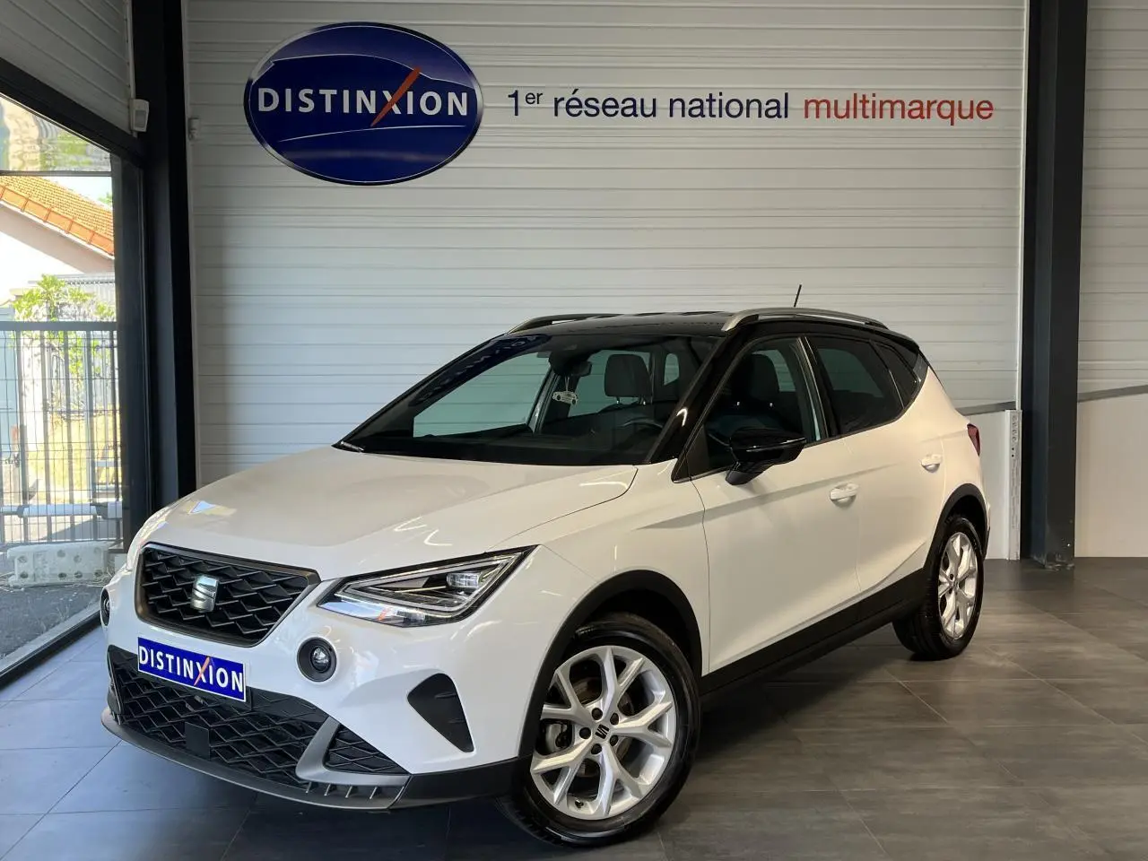 SEAT Arona blanc Nevada 2024 en 3/4 avant droit avec toit noir et jantes alliage 16 pouces en showroom