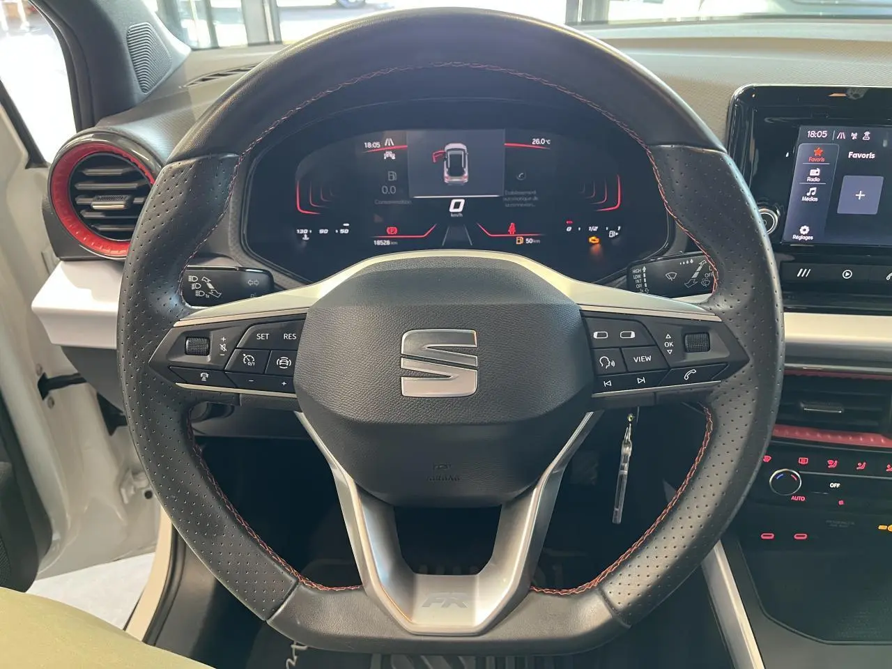 Vue rapprochée du volant sport cuir perforé avec surpiqûres rouges et tableau de bord digital du SEAT Arona blanc Nevada.