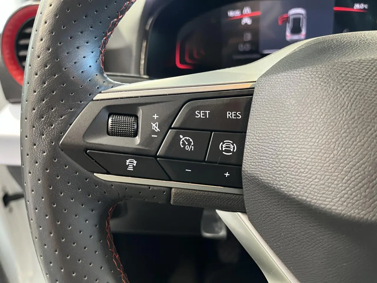 Gros plan sur le volant cuir perforé avec commandes de régulateur et aide à la conduite du SEAT Arona blanc Nevada 2024.