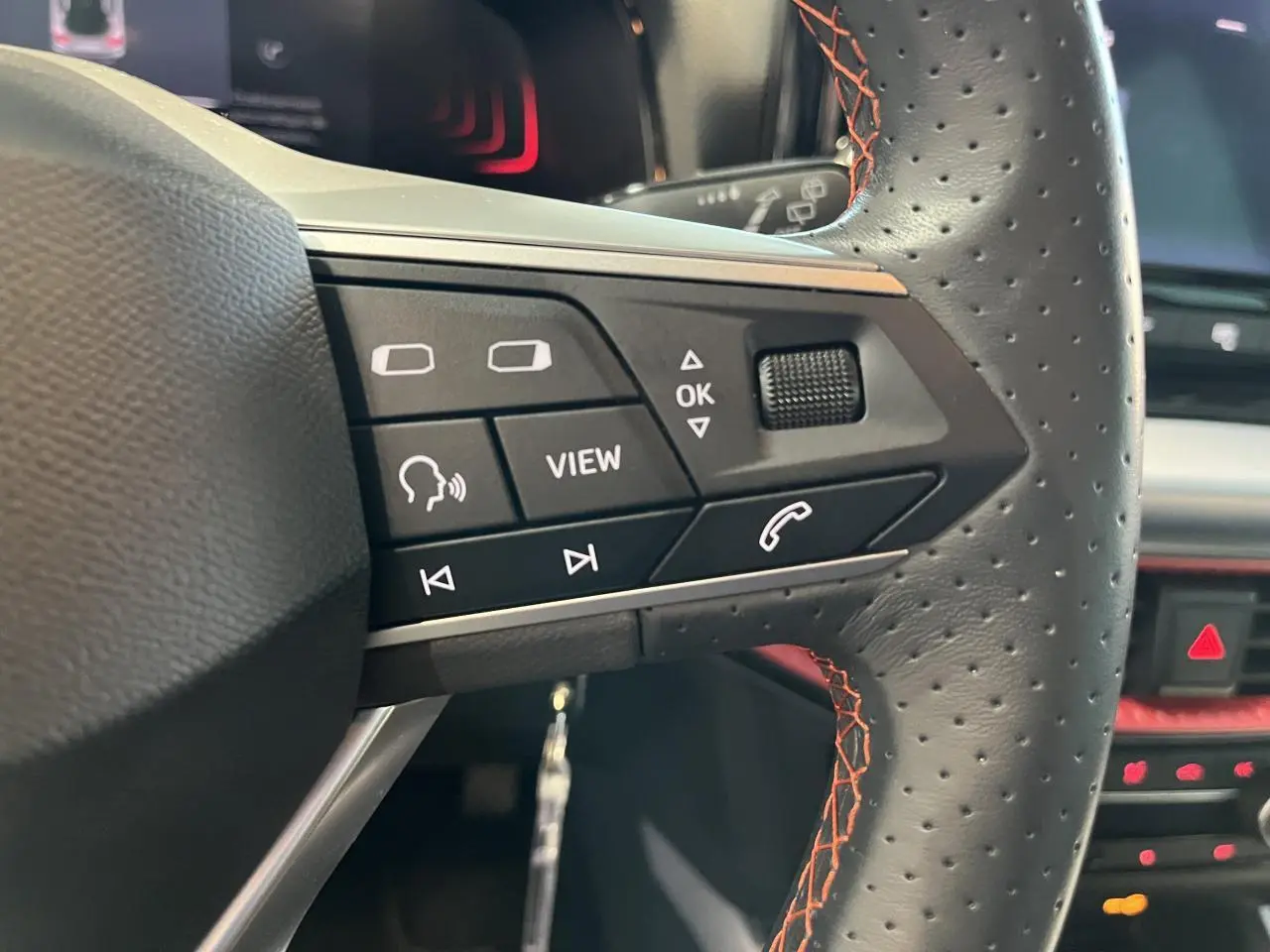 Gros plan sur les commandes du volant sport cuir perforé avec surpiqûres rouges du SEAT Arona blanc Nevada 2024.