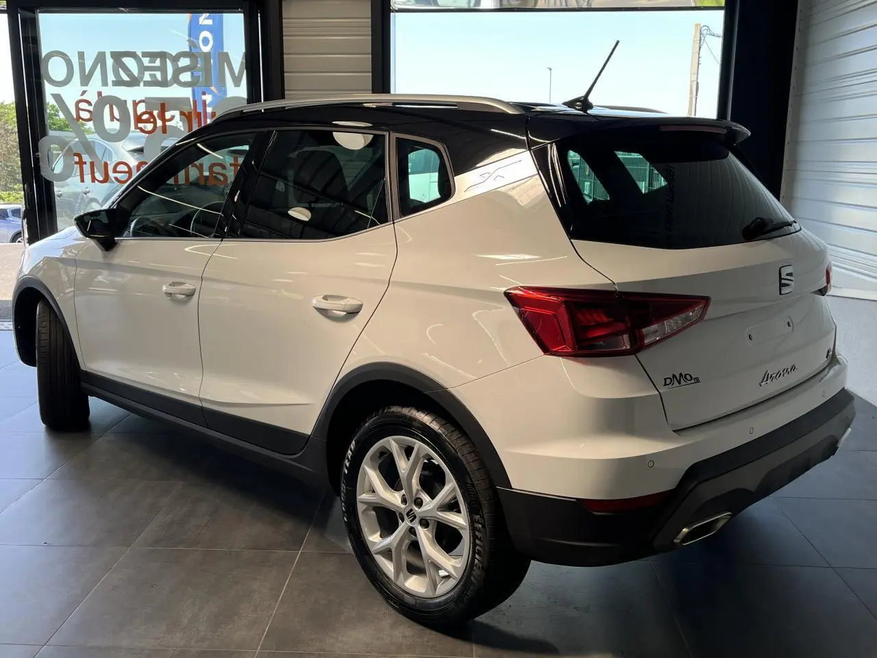 SEAT Arona blanc Nevada vu de 3/4 arrière droit avec toit noir et jantes alliage 16 pouces en showroom.