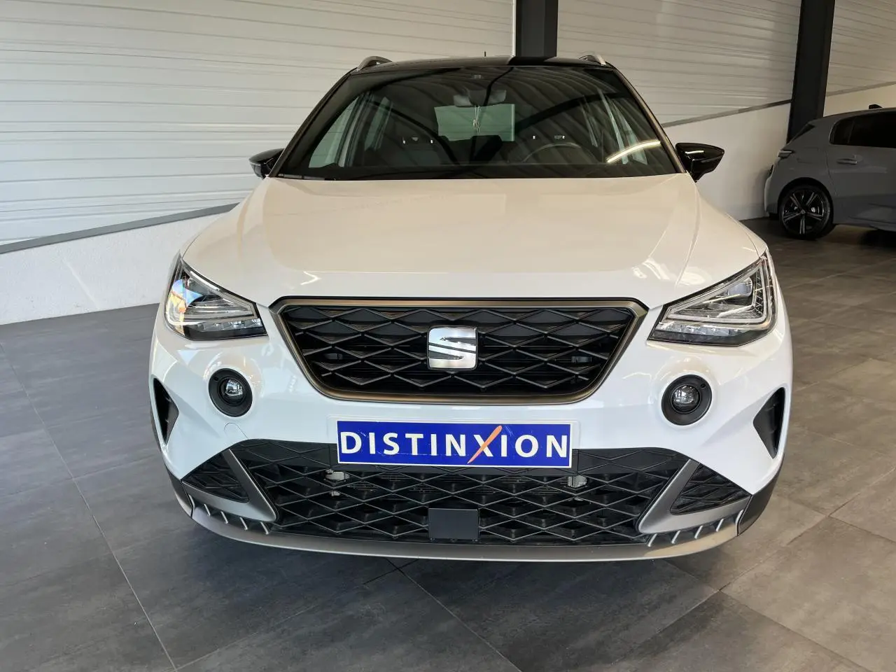 Vue frontale d'un SEAT Arona blanc Nevada avec calandre noire et projecteurs EcoLED dans un showroom.