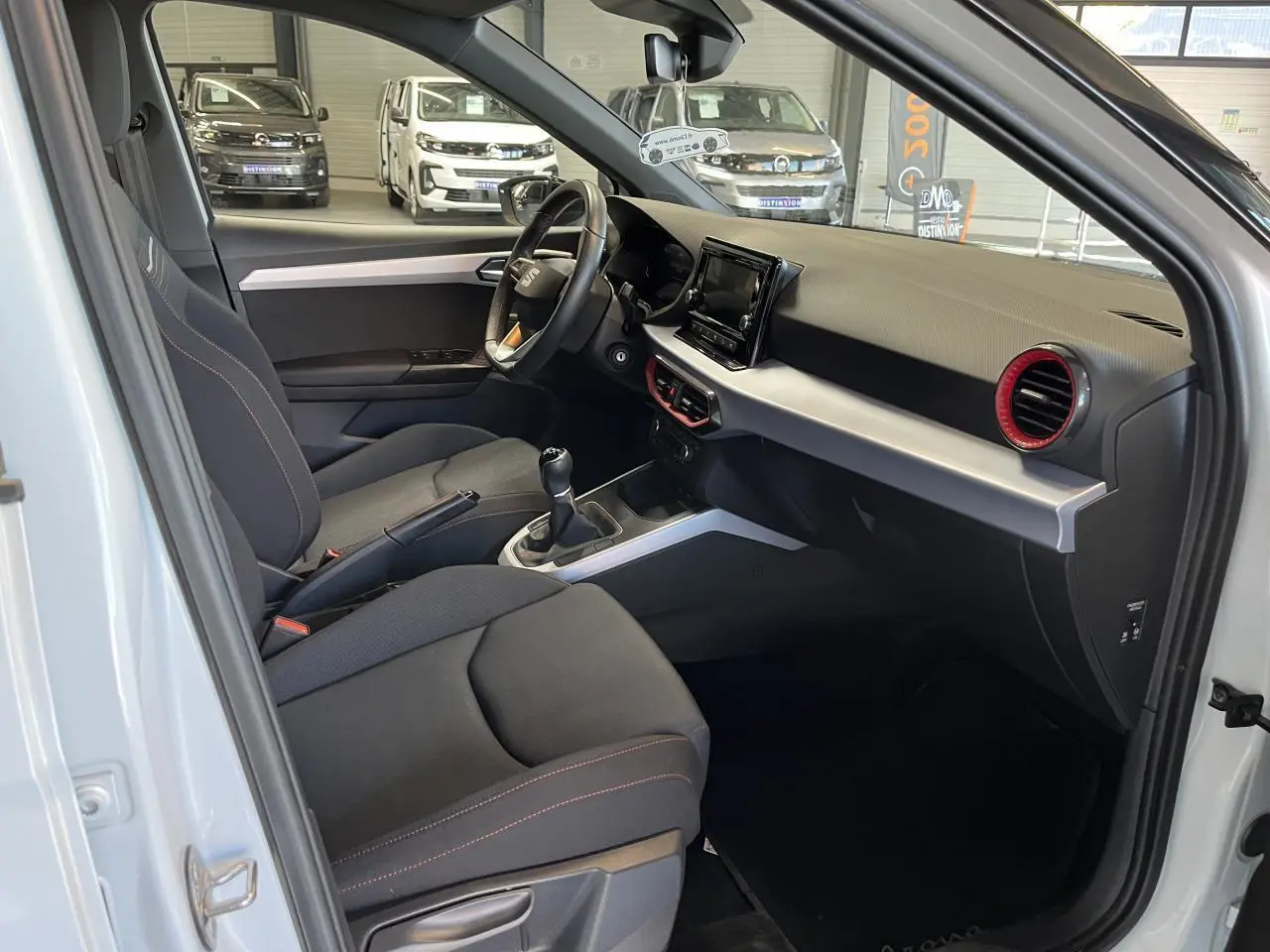 Intérieur côté conducteur du SEAT Arona blanc Nevada 2024, avec tableau de bord noir et aérateurs rouges.