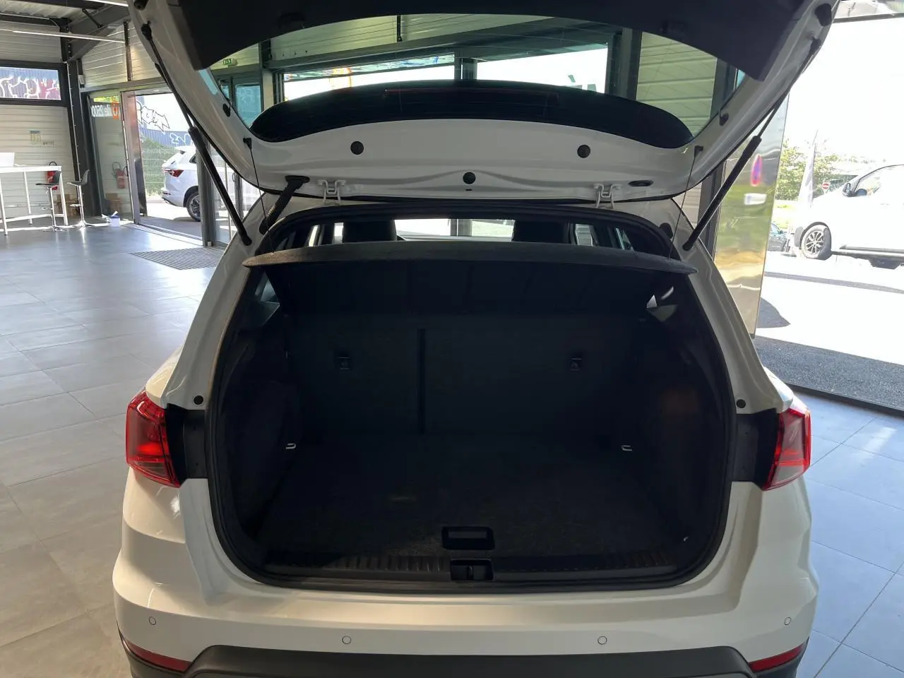 Coffre ouvert vu de l'arrière d'un SEAT Arona blanc Nevada 2024 dans un showroom lumineux.