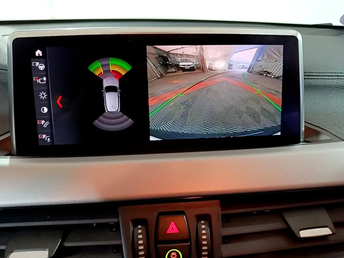 Écran central de la BMW X2 sDrive18i 2023 montrant l’aide au stationnement avec vue caméra arrière et capteurs.