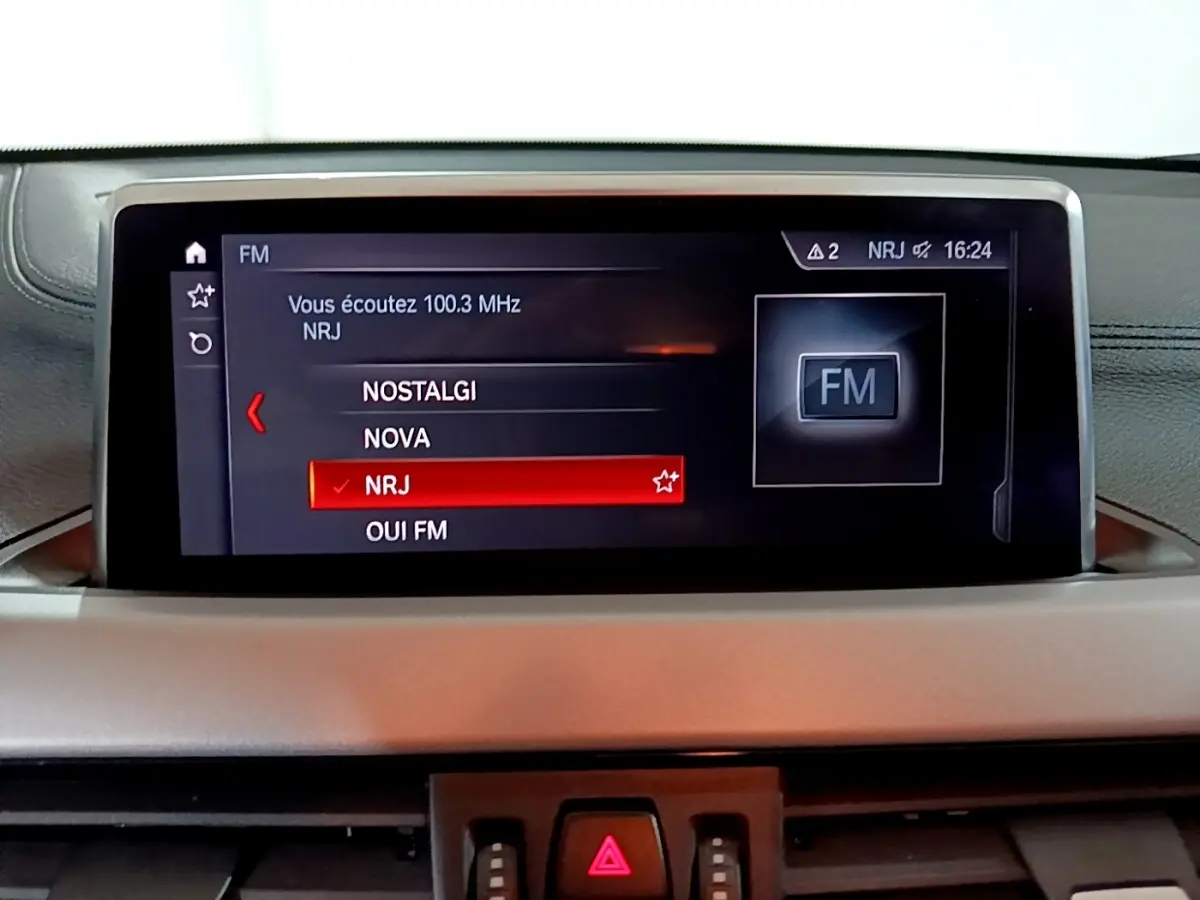 Écran central du tableau de bord du BMW X2 sDrive18i 2023 affichant la sélection radio FM NRJ.