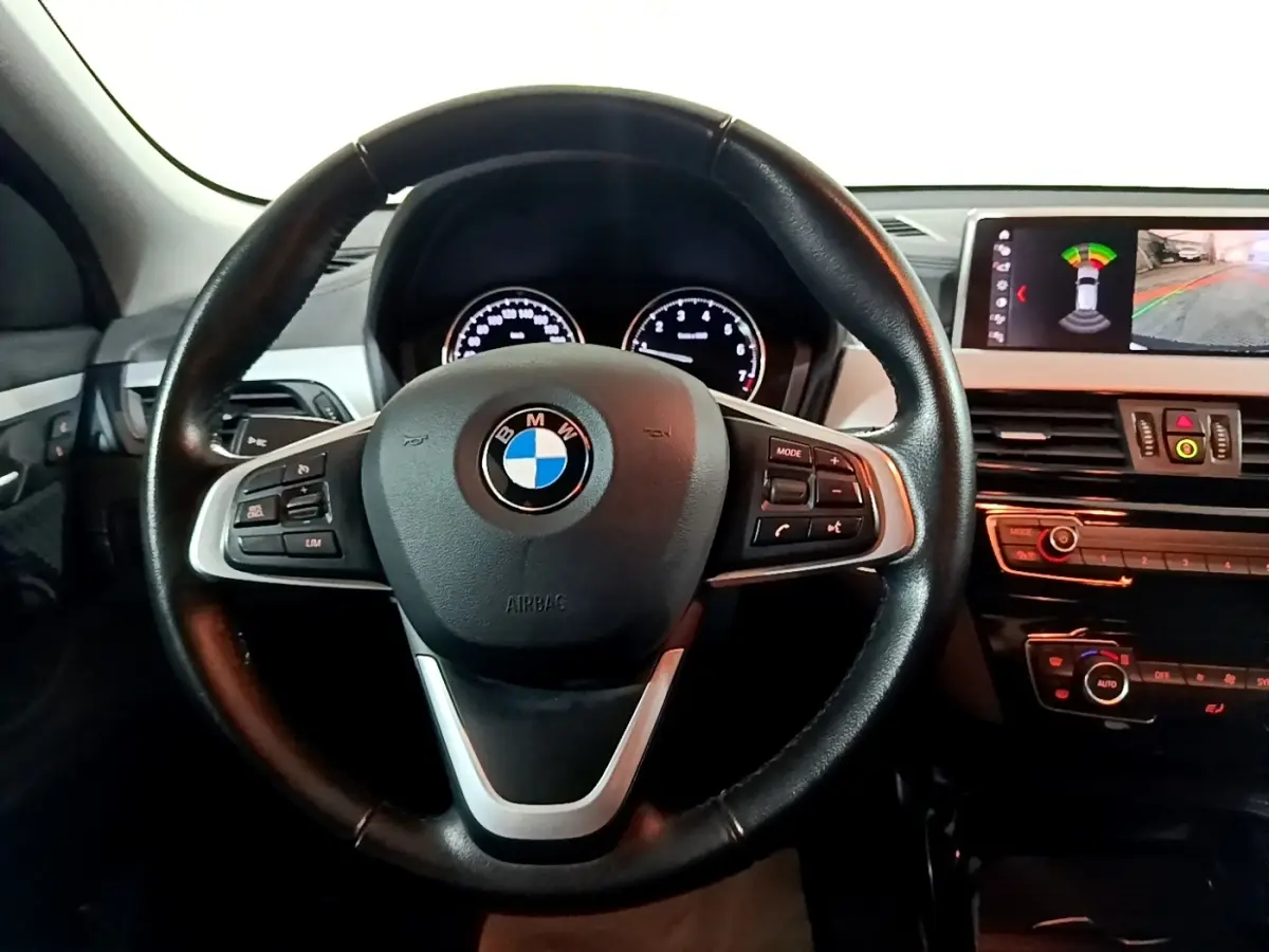 Vue rapprochée du volant cuir et alu noir de la BMW X2 sDrive18i 2023 avec tableau de bord et écran multimédia allumé.