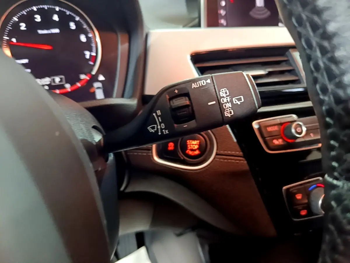 Vue rapprochée du commodo d’essuie-glace et bouton start/stop sur tableau de bord noir d’une BMW X2 2023.