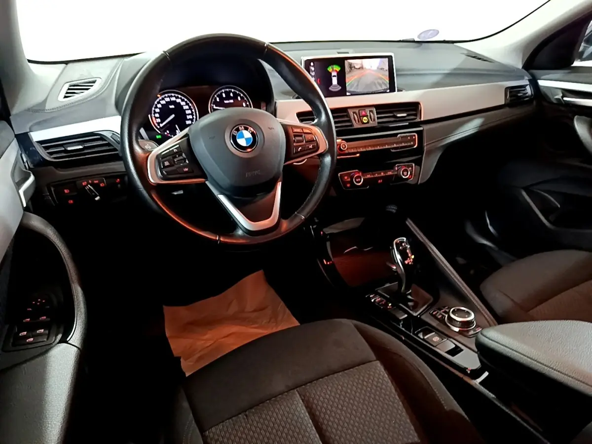 Vue intérieure côté conducteur du BMW X2 sDrive18i 2023, volant cuir alu multifonctions et écran central affichant caméra de recul.