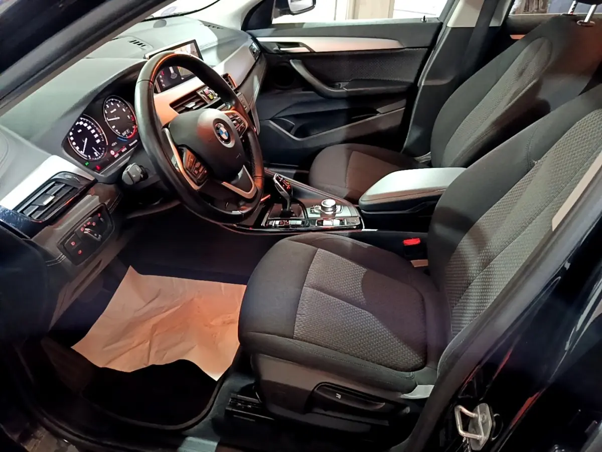 Vue intérieure côté conducteur de la BMW X2 sDrive18i Lounge 2023, sièges noirs et volant cuir multifonctions.