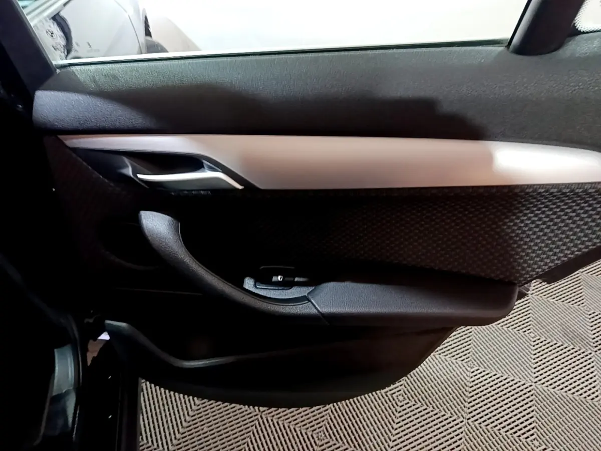 Vue intérieure côté gauche de la porte avant noire de la BMW X2 sDrive18i Lounge avec poignée alu et habillage texturé.