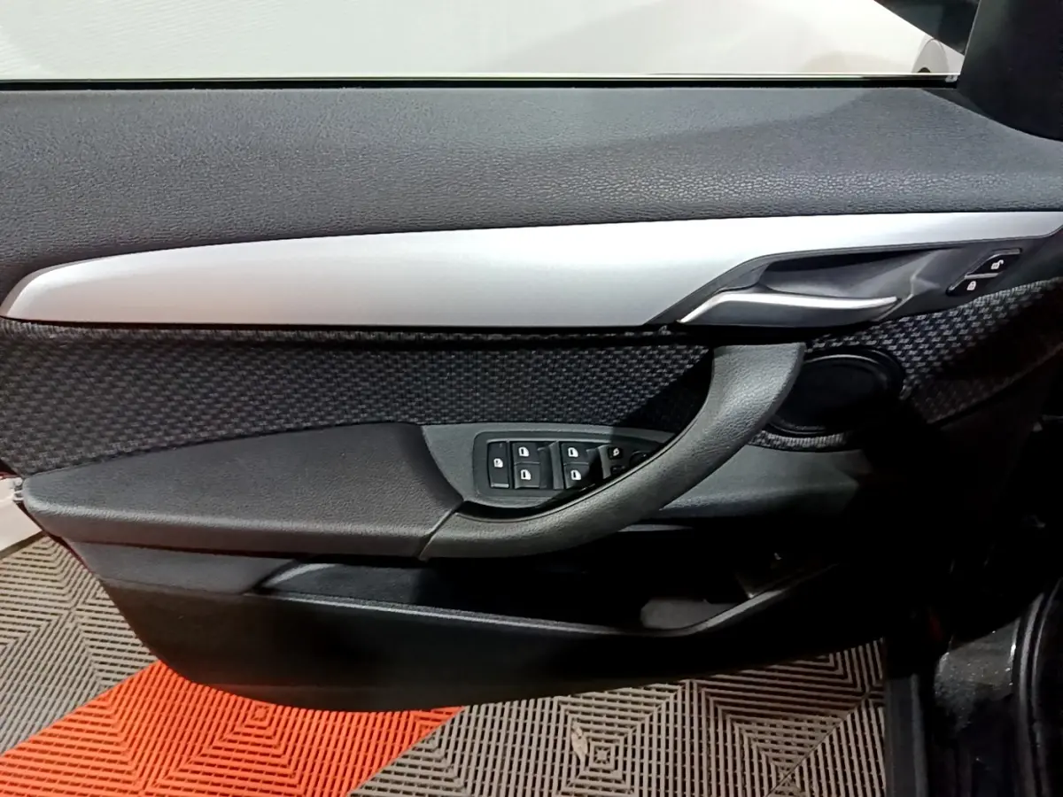 Gros plan sur la porte côté conducteur de la BMW X2 noire, mettant en valeur la poignée, les commandes de vitres et la finition alu.
