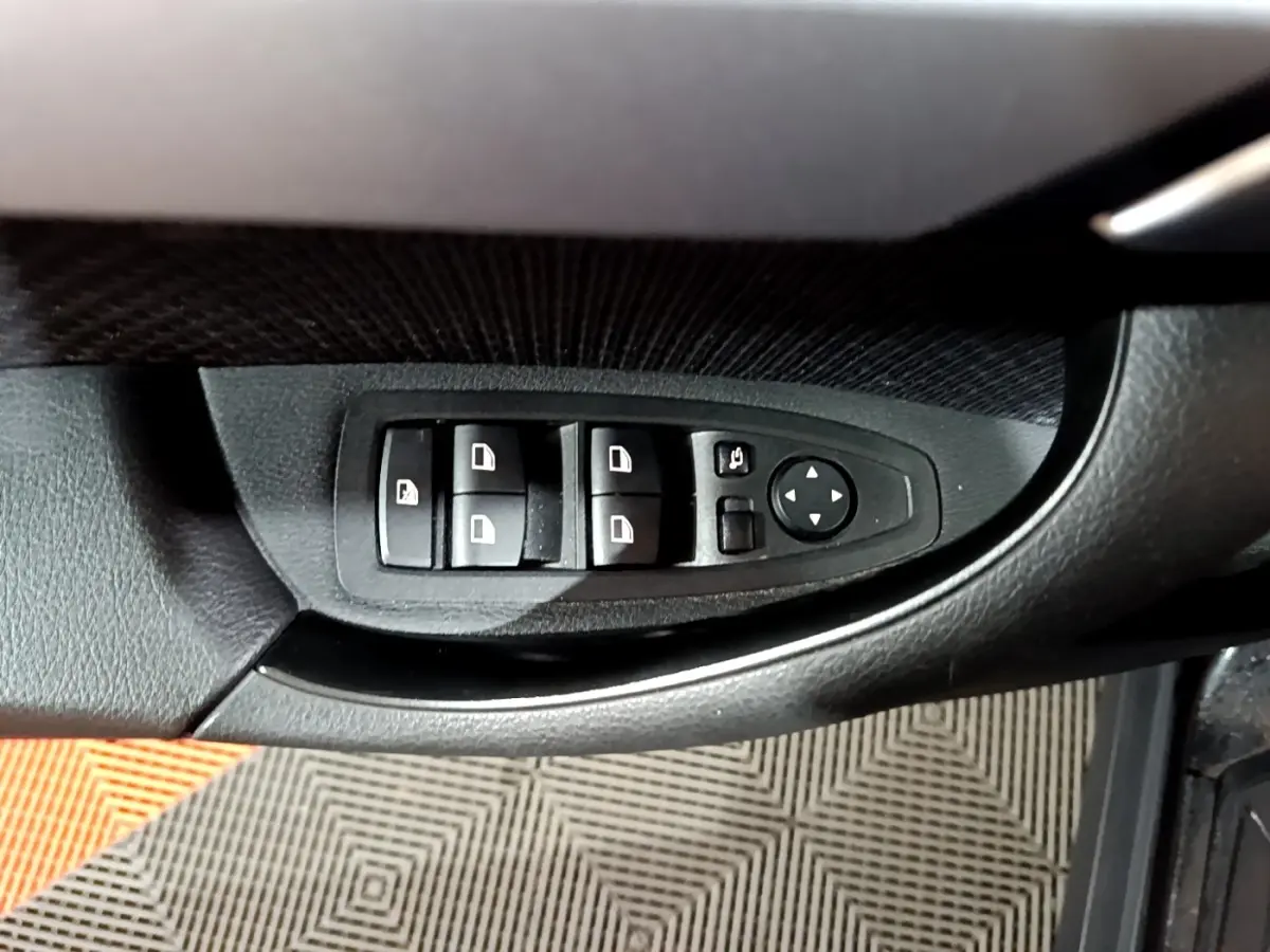 Gros plan sur les commandes de lève-vitres et rétroviseurs côté conducteur d’une BMW X2 noire 2023.