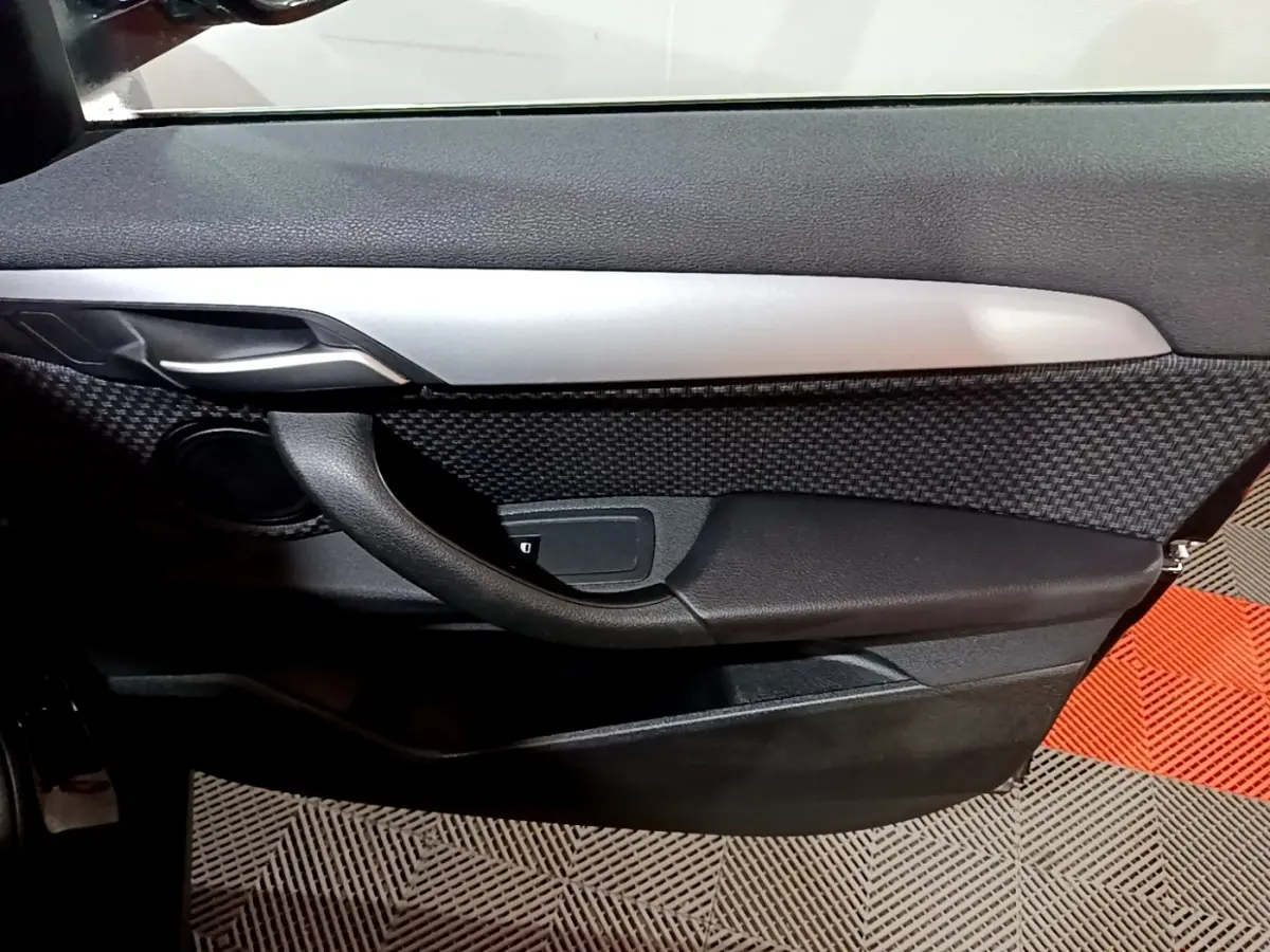 Gros plan sur la porte côté gauche de la BMW X2 sDrive18i Lounge 2023, avec garniture noire et insert argenté.