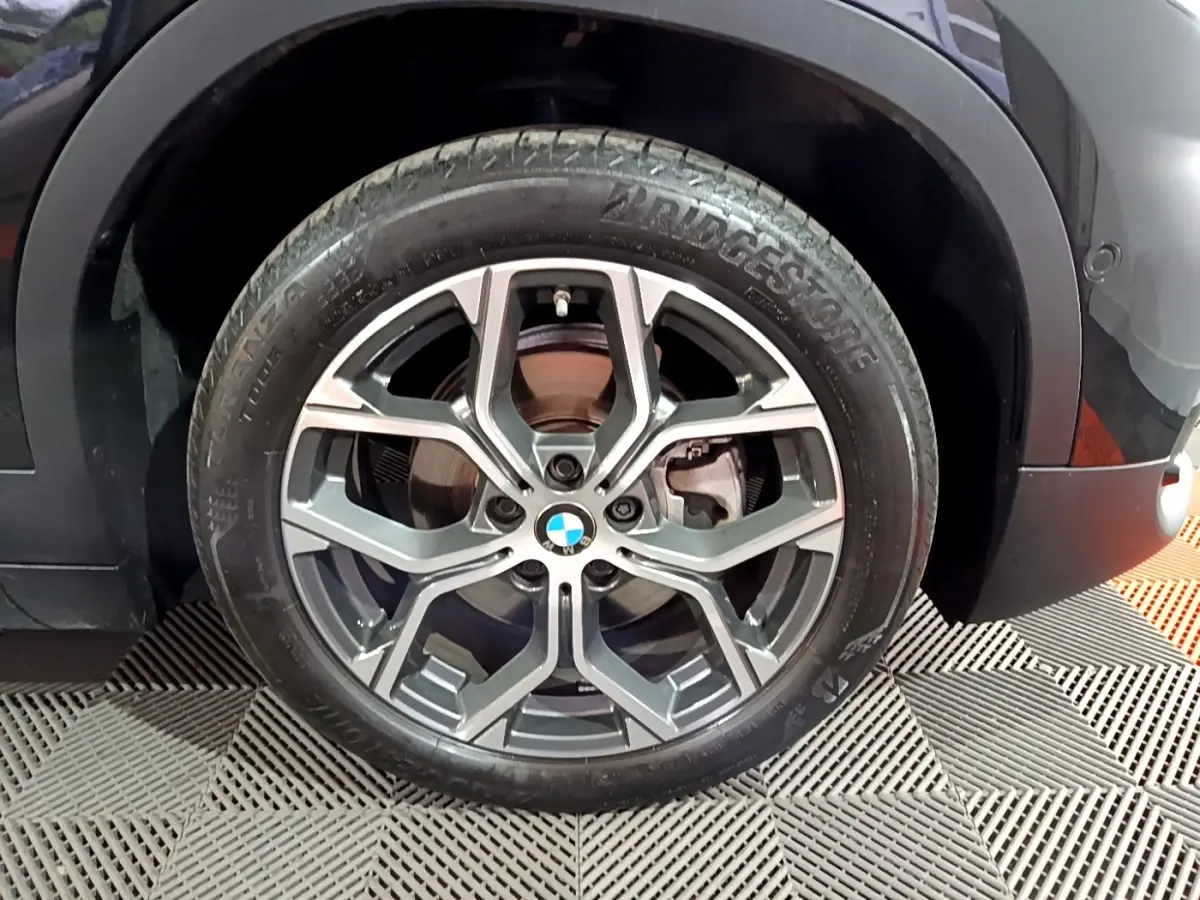 Gros plan sur la roue avant gauche noire d’un BMW X2 2023 avec jante alliage à design moderne.