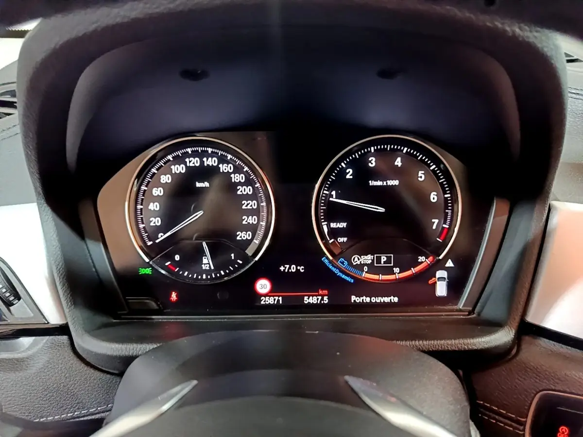 Tableau de bord numérique de BMW X2 sDrive18i 2023, affichage vitesse et compte-tours avec alertes visibles.