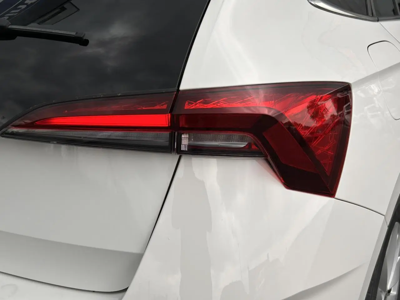 Gros plan sur le feu arrière droit rouge vif d'une SKODA SCALA 2025 blanc Candy avec lunette arrière surteintée.
