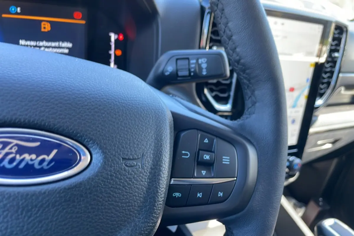 Gros plan sur le volant en cuir noir du Ford Ranger 2025, avec commandes intégrées et tableau de bord numérique en arrière-plan.