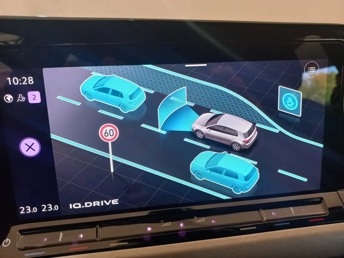 Affichage tactile intérieur montrant la Volkswagen Golf grise en vue 3D avec voitures bleues et panneau 60 km/h.