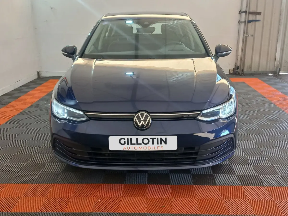 Vue frontale d'une Volkswagen Golf bleu nuit avec phares LED allumés dans un garage.