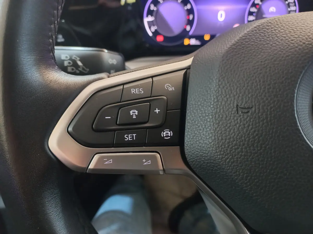 Gros plan sur les commandes du volant côté gauche d'une Volkswagen Golf bleue, tableau de bord numérique en arrière-plan.