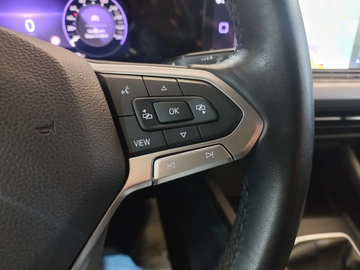 Gros plan sur les commandes du volant côté gauche en cuir noir de la Volkswagen Golf bleue 2022, tableau de bord numérique en arrière-plan.