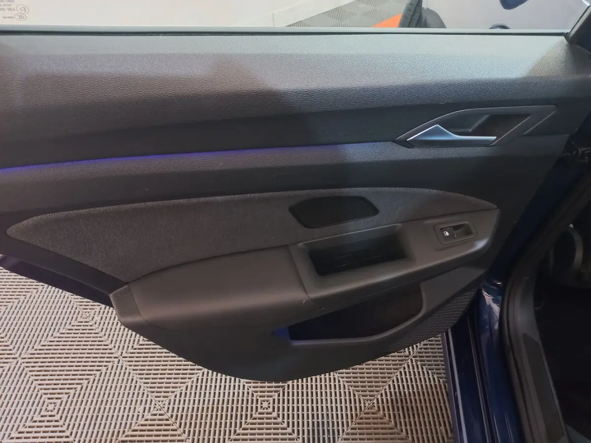 Vue rapprochée de la porte avant droite bleu foncé d'une Volkswagen Golf 2022 avec garniture noire et bouton de verrouillage électrique.